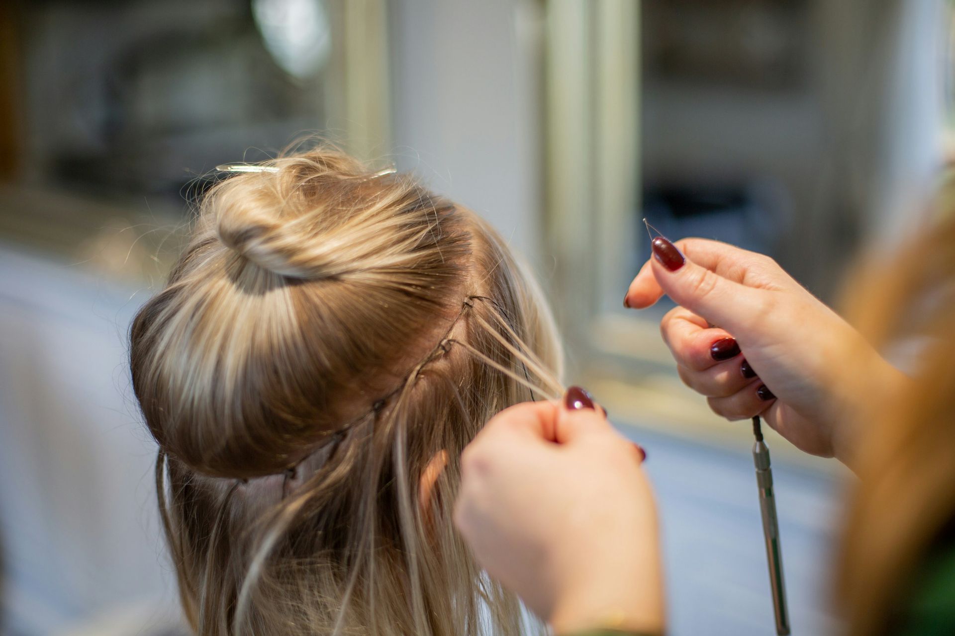 Hands applying hair extensions to blonde hair